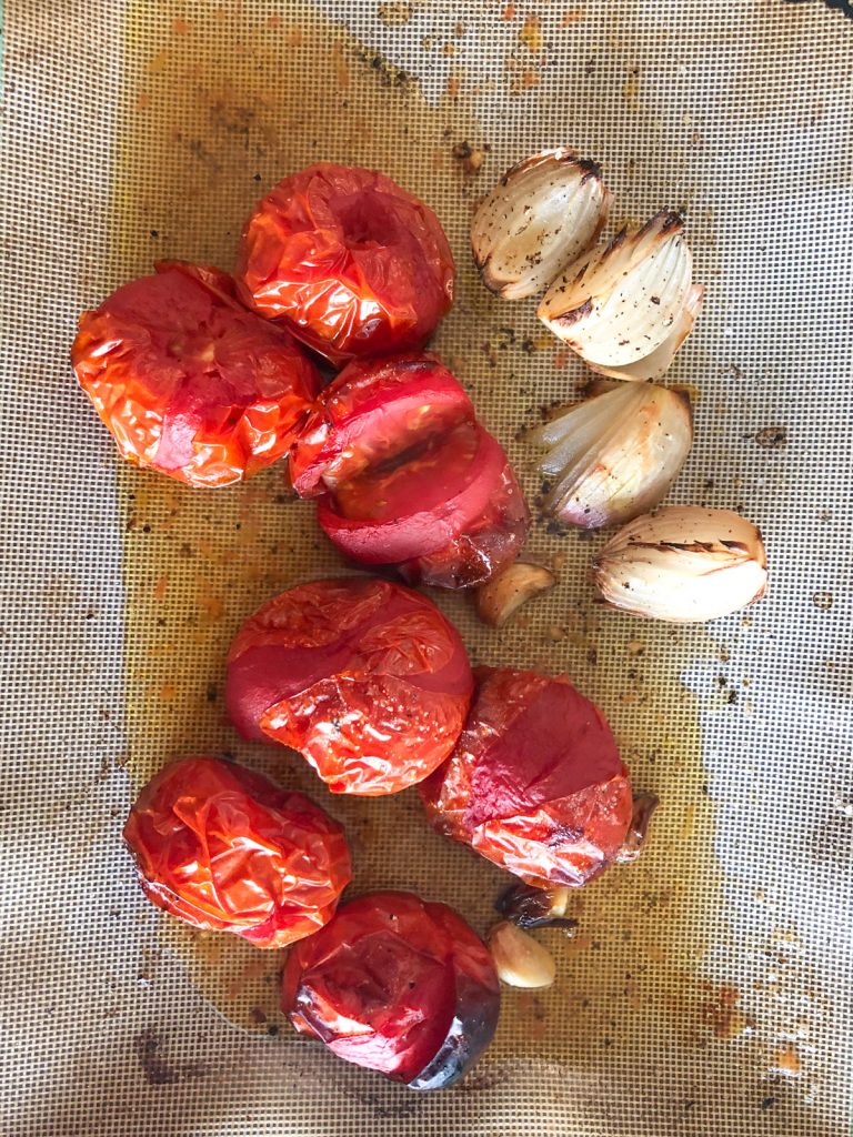 Roasted tomatoes, onions and garlic on a baking tray with olive oil, salt and black pepper.