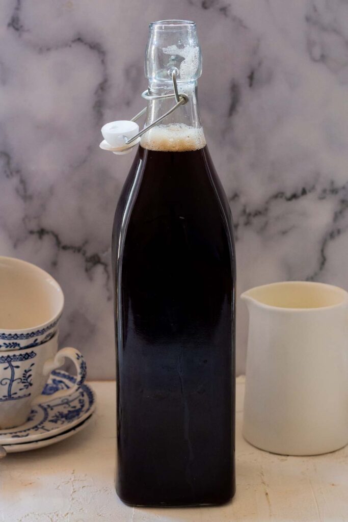 Two tea cups, a glass bottle filled with Kashmiri chai kahwa, and a milk jug.