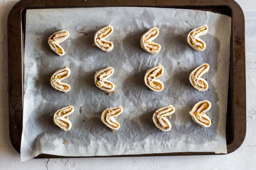 A top down shot of a baking tray lined with parchment on which are raw puff pastry palmiers.