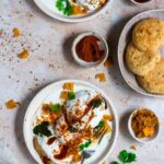 A plate of lentil fritters with yoghurt, with more fritters on the side.