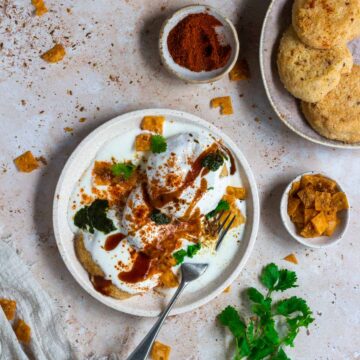 A plate of lentil fritters with yoghurt, with more fritters on the side.