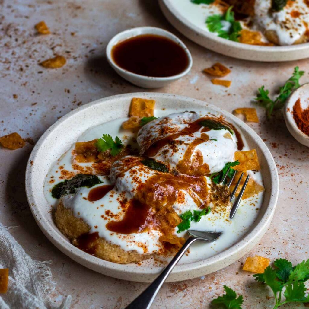 A plate of lentil fritters with yoghurt, with more fritters on the side.