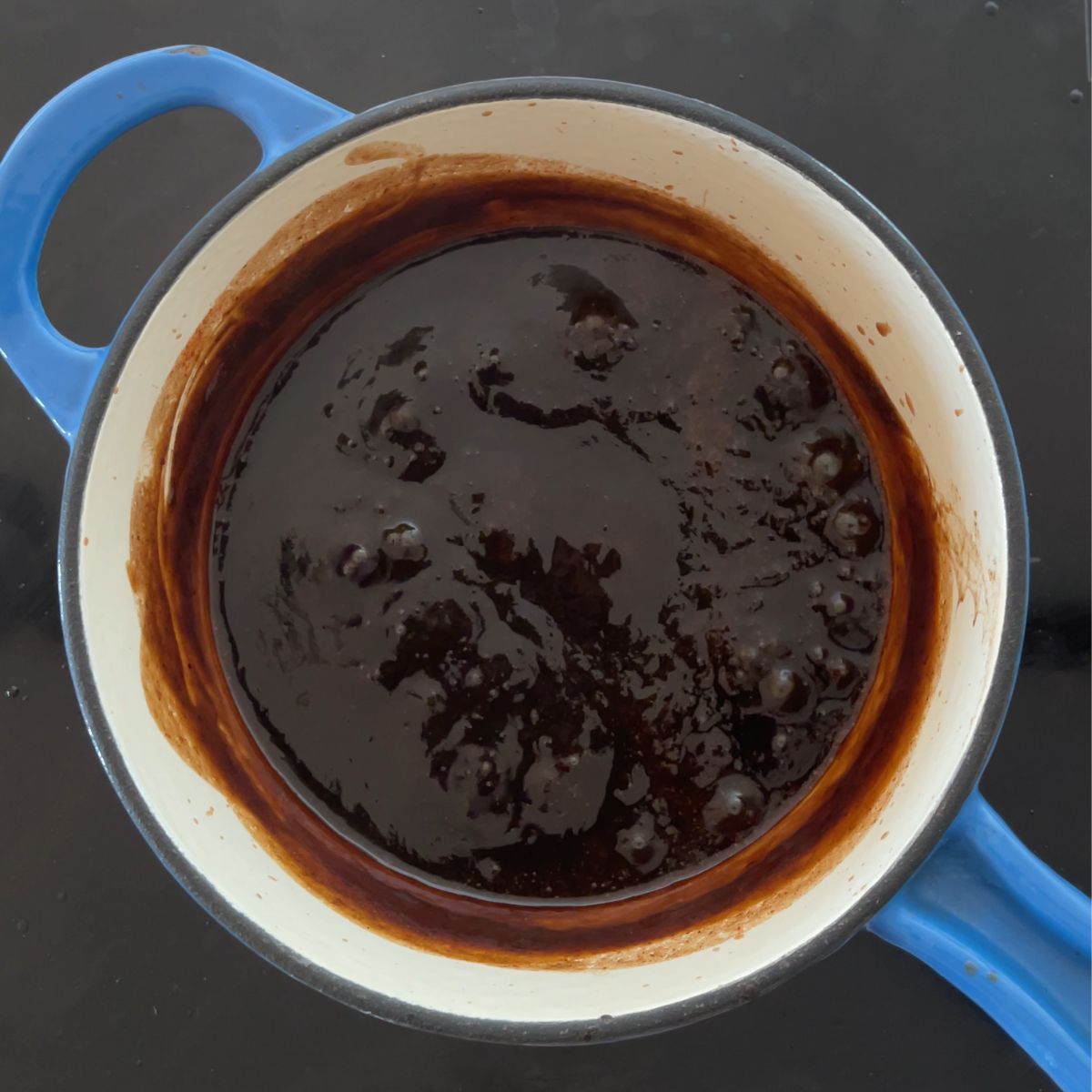 Imli / tamarind chutney is being cooked in a blue and white saucepan. 