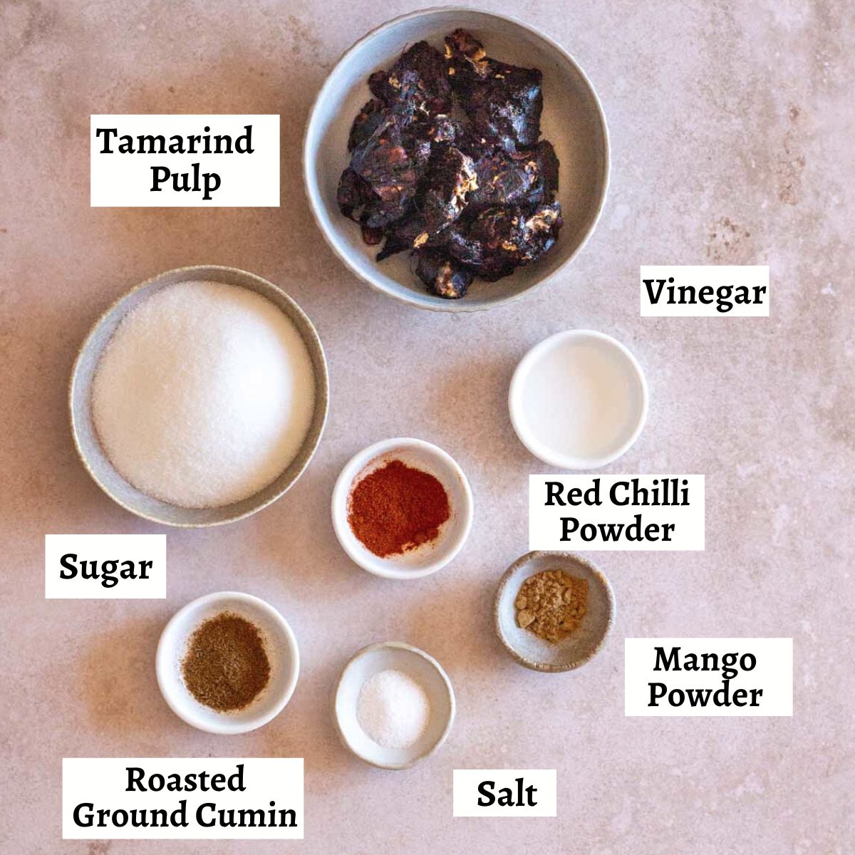 Ingredients for imli chutney in bowls with labels to identify what they are. 