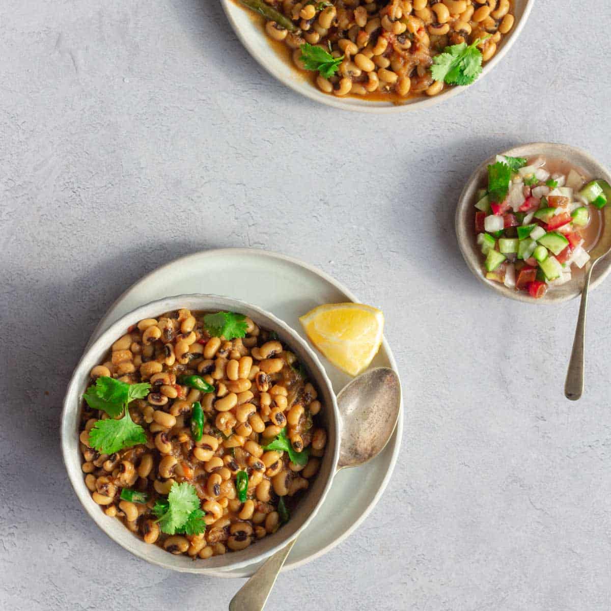 A bowl of lobia masala (black eyed peas curry) with a spoon and lemon next to it. 