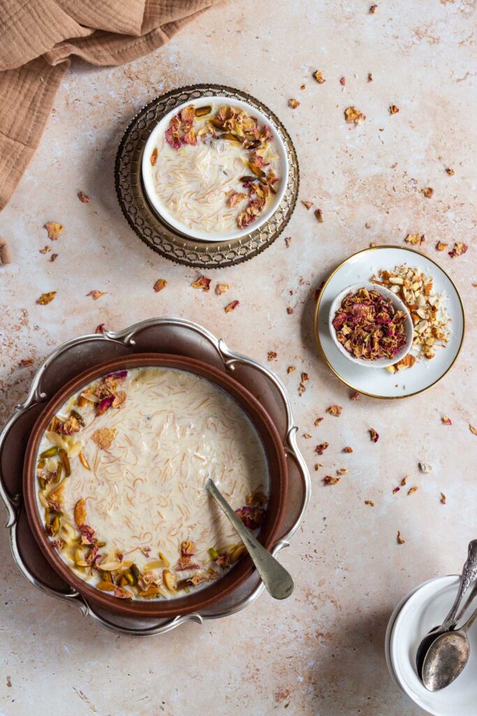 Three bowls of sheer khurma garnished with nuts and rose petals.