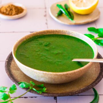 A bowl of cilantro chutney with mint in a bowl, with a small spoon in it.