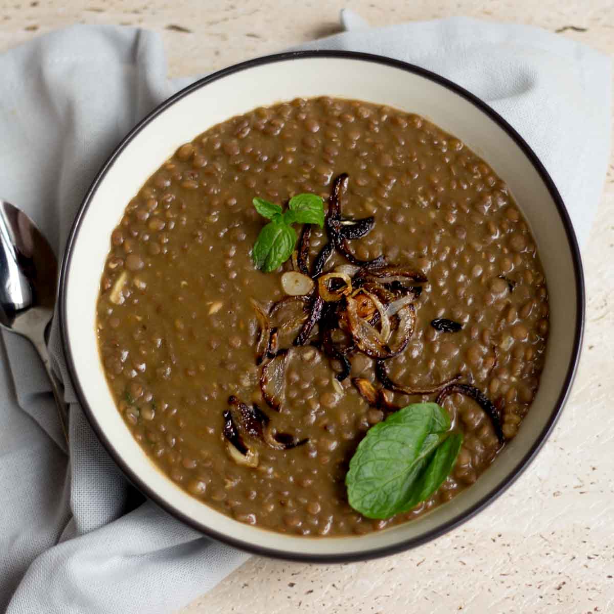 A bowl of kaali daal (black gram lentils) topped with onions and mint leaves.