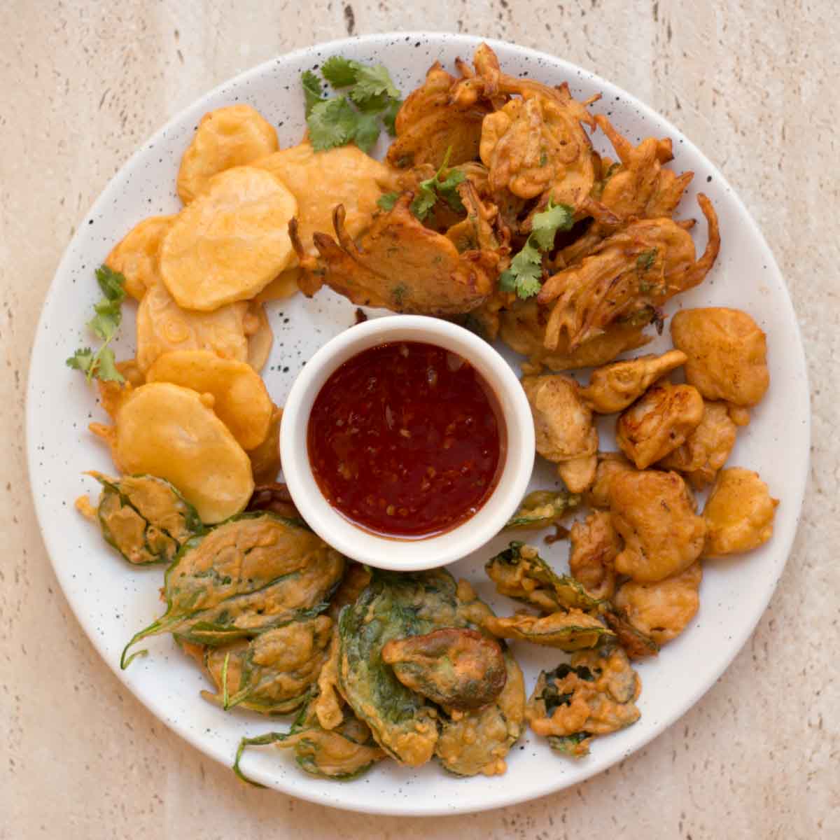 A plate of pakoras (gram flour fritters) with a bowl of tomato sauce.