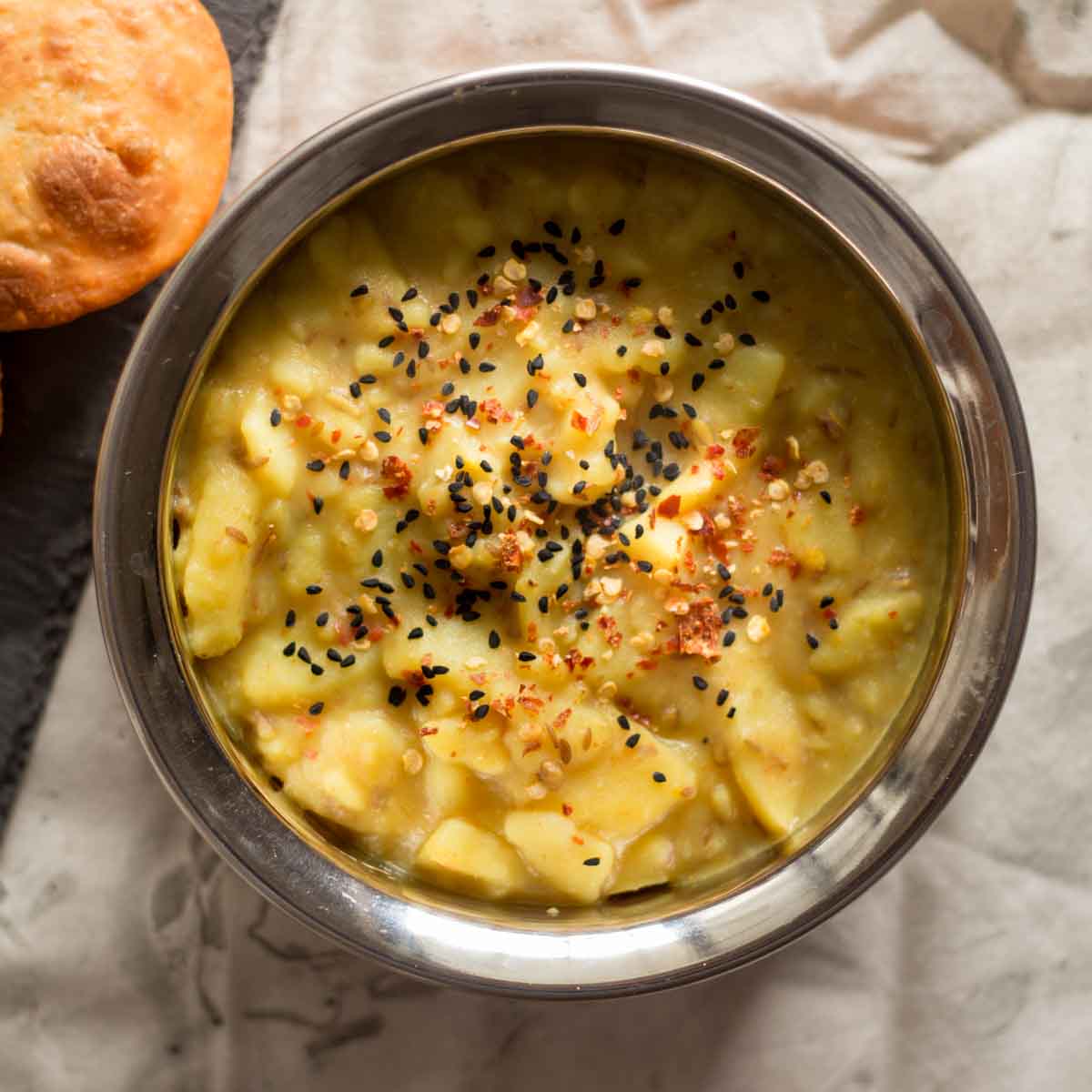 A steel bowl filled with aloo ki tarkari (Pakistani spiced potato curry).