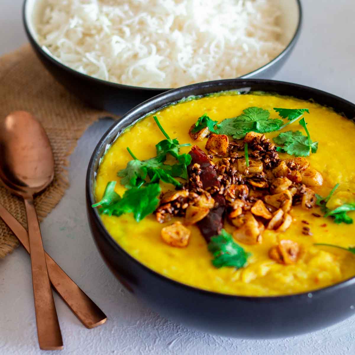 A bowl of moong masoor daal in a bowl with rice in the background.