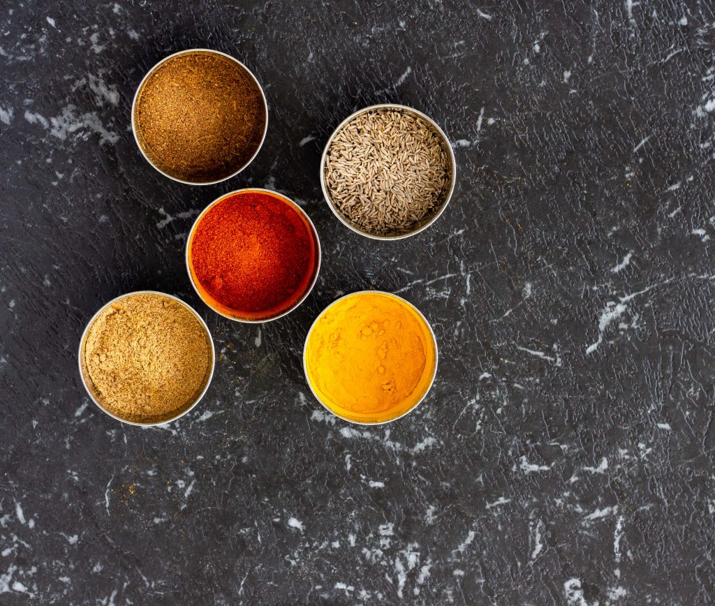 Spices that are regularly used in a Desi kitchen placed in small steel bowls- they include red chilli powder, coriander powder, turmeric, cumin seeds and garam masala. 