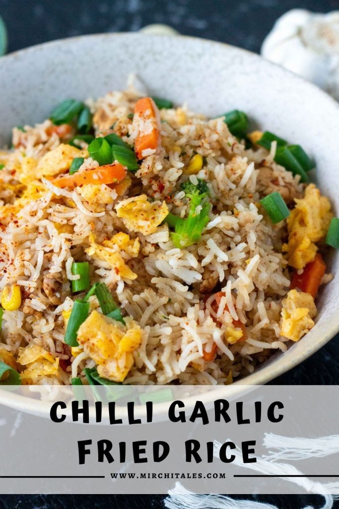 A white bowl filled with chilli garlic fried rice with eggs, vegetable and sliced chicken, and topped with spring onions. Below the bowl is text that states "chilli garlic fried rice" along with the website name - www.mirchitales.com