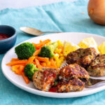 A plate with turkey rissoles, lemon wedges and steamed carrots, broccoli and corn.