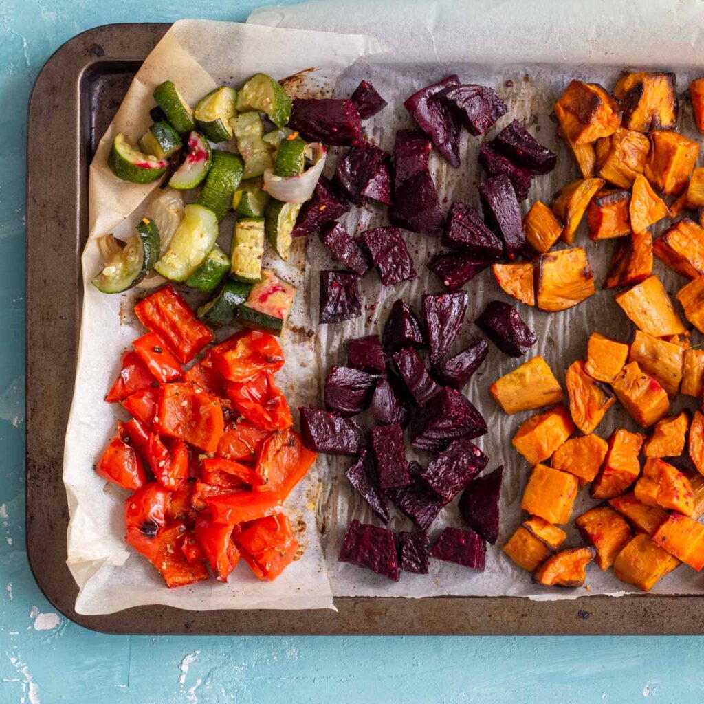 A baking tray with roasted vegetables on it cut in cubes.