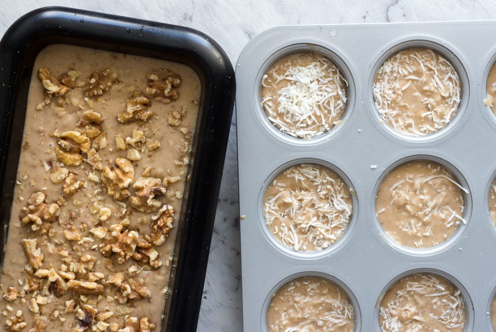 Ripe bananas are turned into banana bread. There's a rectangle loaf pan with about 50% of it visible - it's filled with banana bread batter topped with walnuts. Next to the pan is a muffin pan with just 6 muffin cups visible. They are filled with banana bread batter, topped with coconut. 