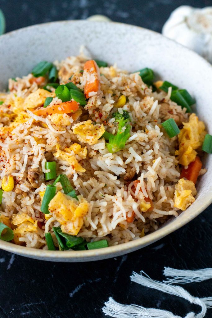 A bowl of fried rice made with chicken, vegetables and scrambled egg on top. 