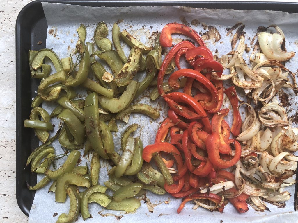 A tray of roasted vegetables - on the left end is roasted green capsicum or green bell pepper, and in the middle are roasted red capsicum. or red bell pepper. On the right are roasted and sliced onions.