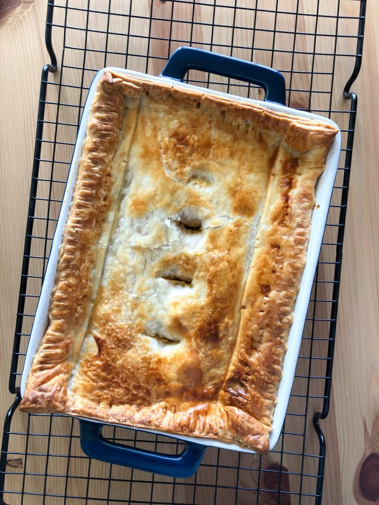 A chicken pot pie with puff pastry on top is made in a rectangle dark blue ceramic glass tray. The tray is kept on a wire rack.