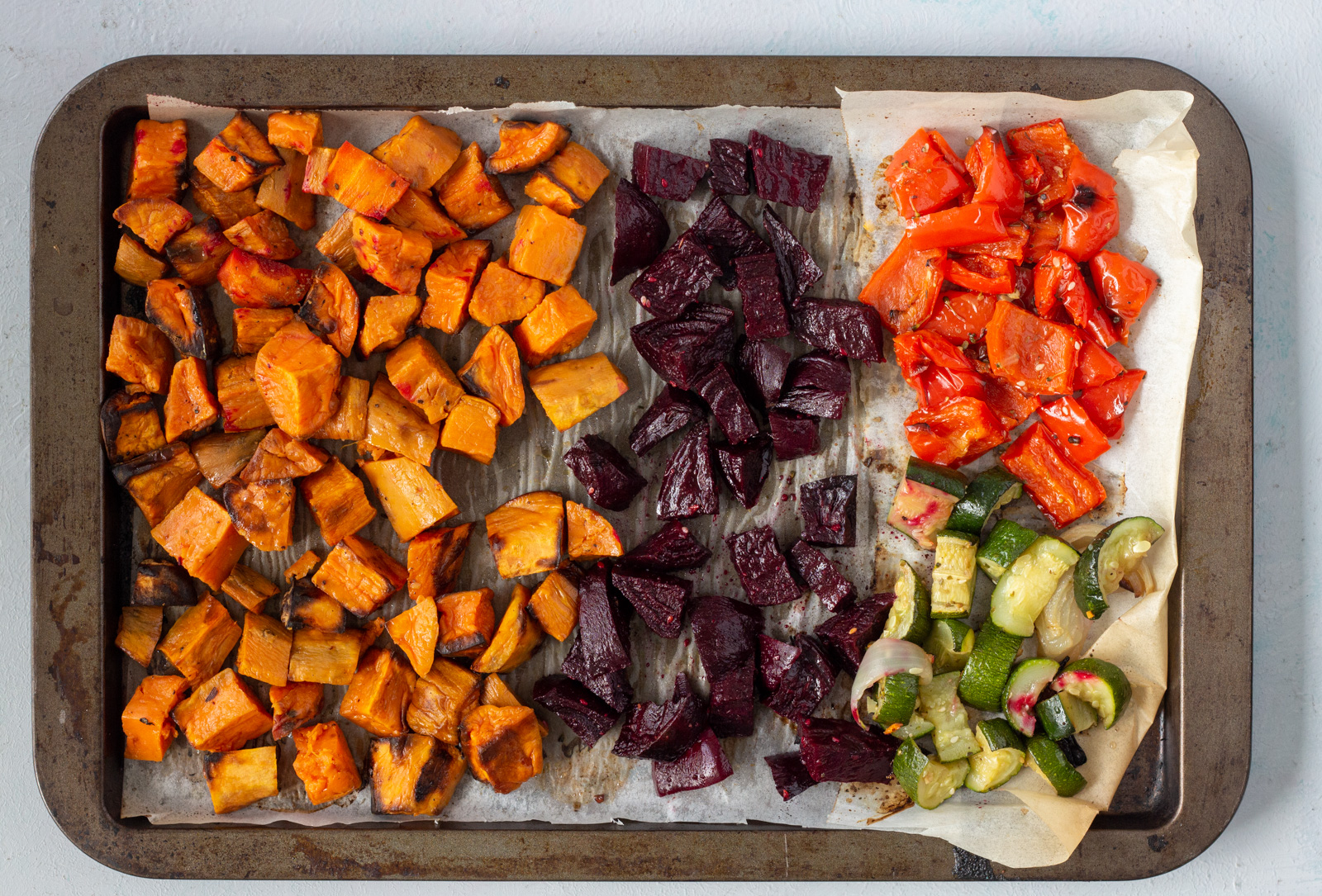 A baking tray with roasted vegetables on it cut in cubes - the vegetables are sweet potato, beetroot, red capsicum / red bell pepper and zucchini. 