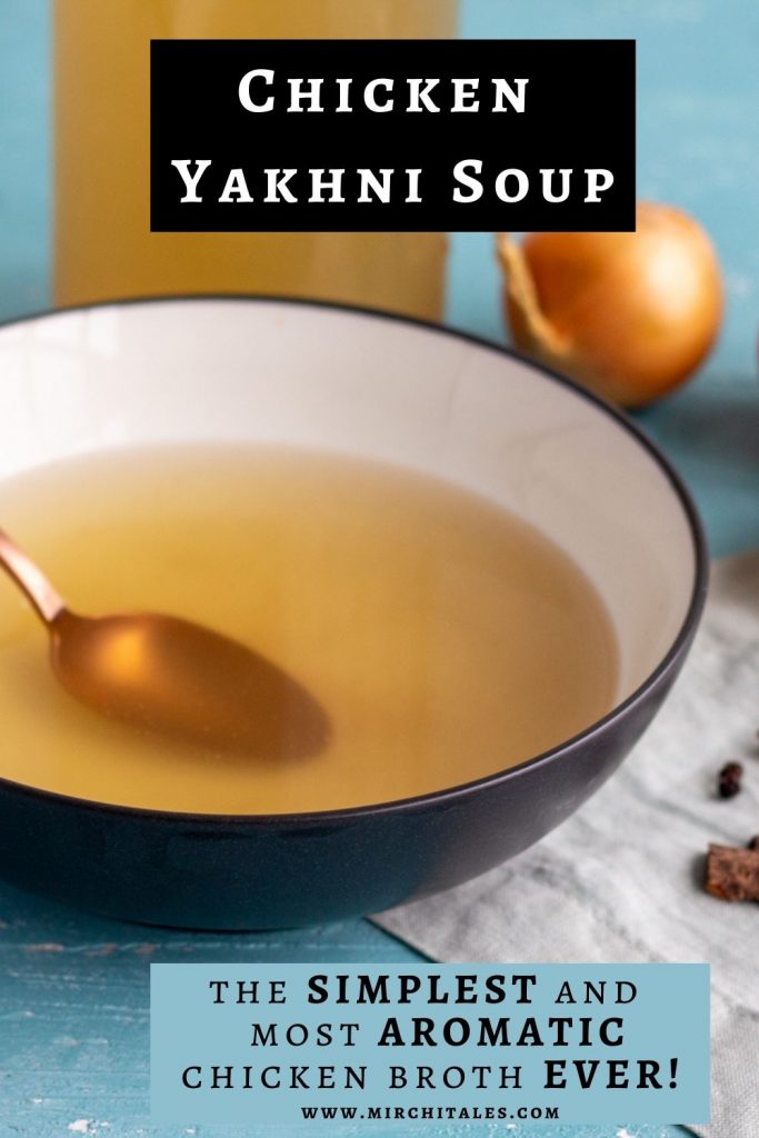 A bowl of chicken yakhni or Pakistani and Indian style chicken broth. The yakhni is in a black bowl with a glass bottle of broth in the background, along with onion and garlic and whole spices to the right.