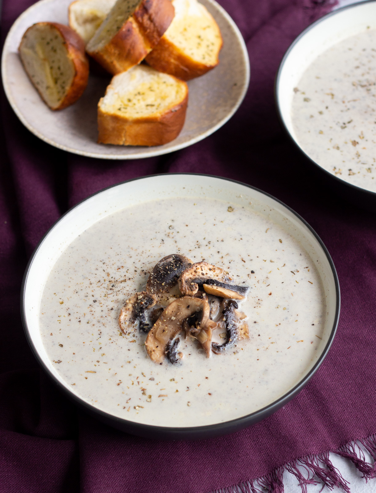 A bowl of creamy mushroom soup with another bowl at the back, along with garlic bread.