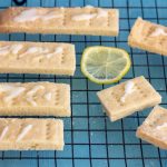 7 lemon and cardamom shortbread cookies on a baking tray, with slices of lemon around the cookies. On top of the shortbread cookies is a lemon glaze.