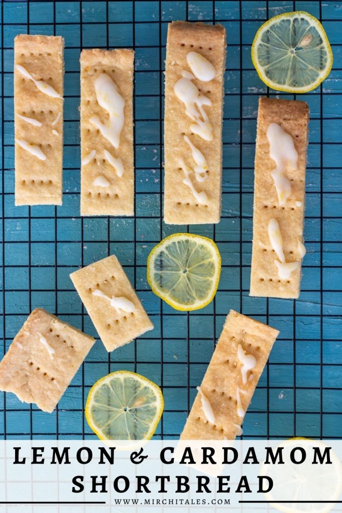 7 lemon and cardamom shortbread cookies on a baking tray, with slices of lemon around the cookies. On top of the shortbread cookies is a lemon glaze.