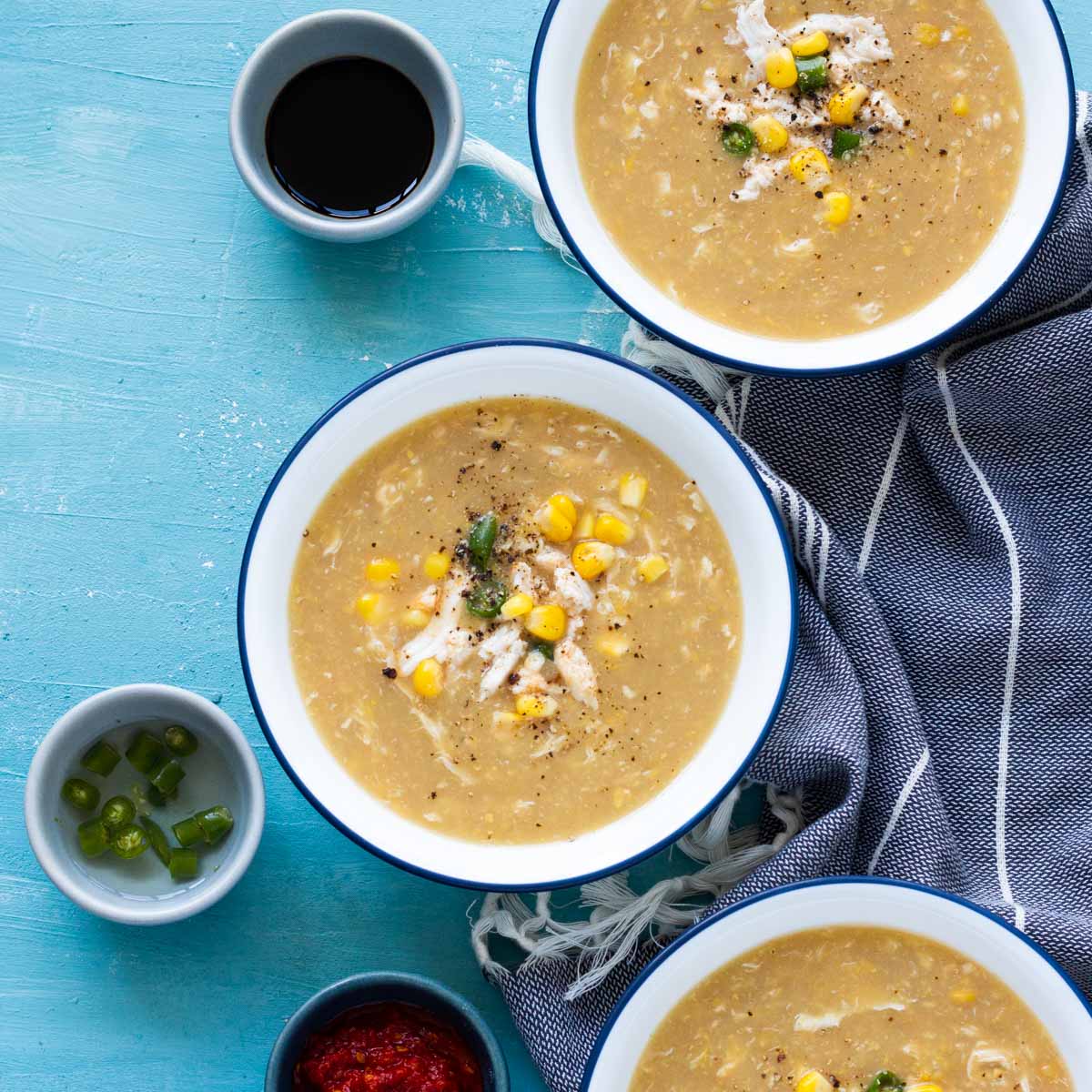 3 bowls of Chinese chicken corn soup on a blue board.