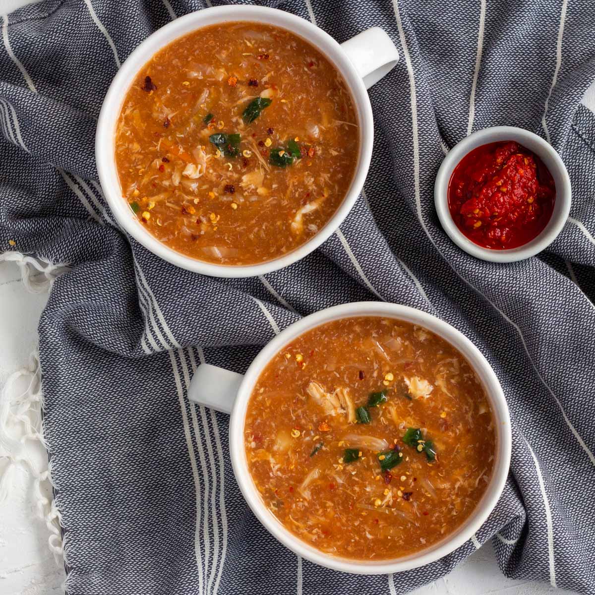 Two bowls of chicken hot and sour soup with a bowl of red chili paste next to the bowls.