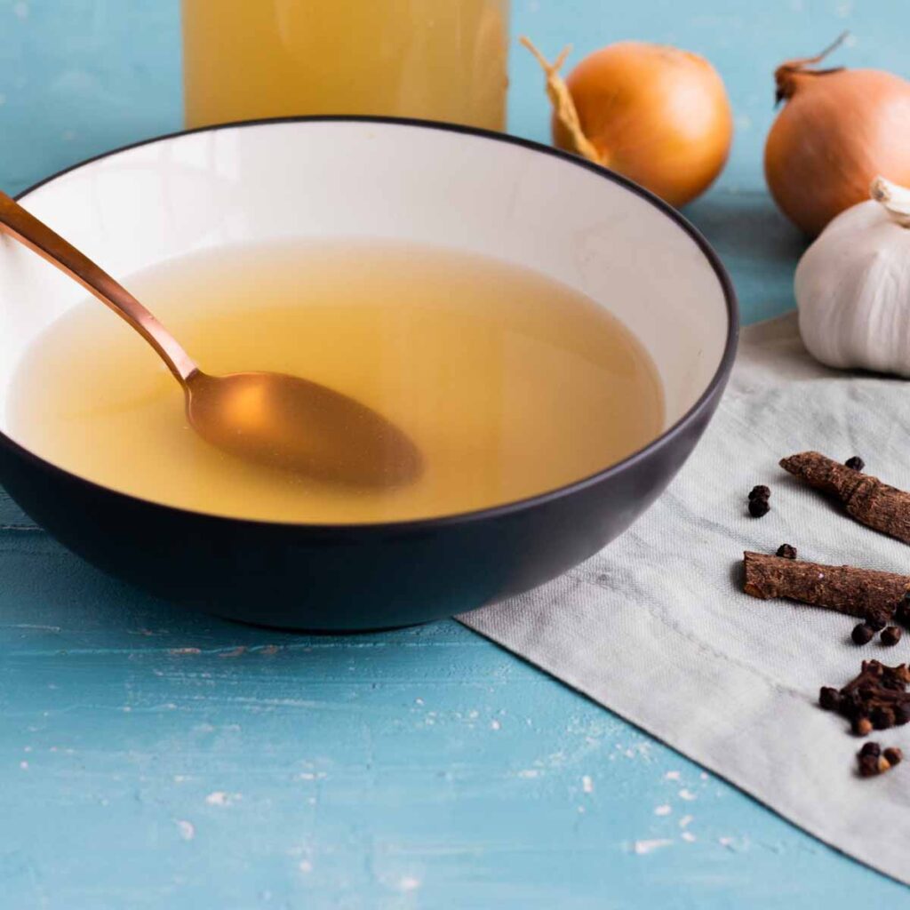 A bowl of chicken yakhni (chicken broth) with a spoon in it.