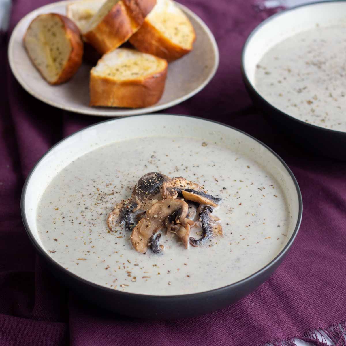 A bowl of creamy mushroom soup with another bowl at the back, along with garlic bread.