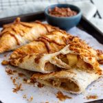 Four apple biscoff turnovers on a baking tray.