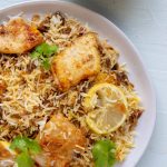 A plate of Pakistani style fish biryani with raita in the background.