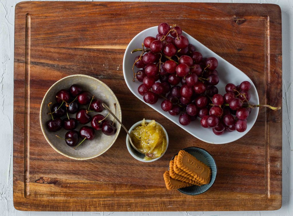 Sweet elements laid out to add to a cheese board - grapes, cherries, mango chutney and Lotus biscuits. 