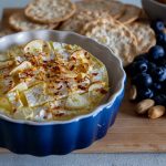 Baked brie with garlic and chili in a cheese board which has blueberries, crackers and nuts.