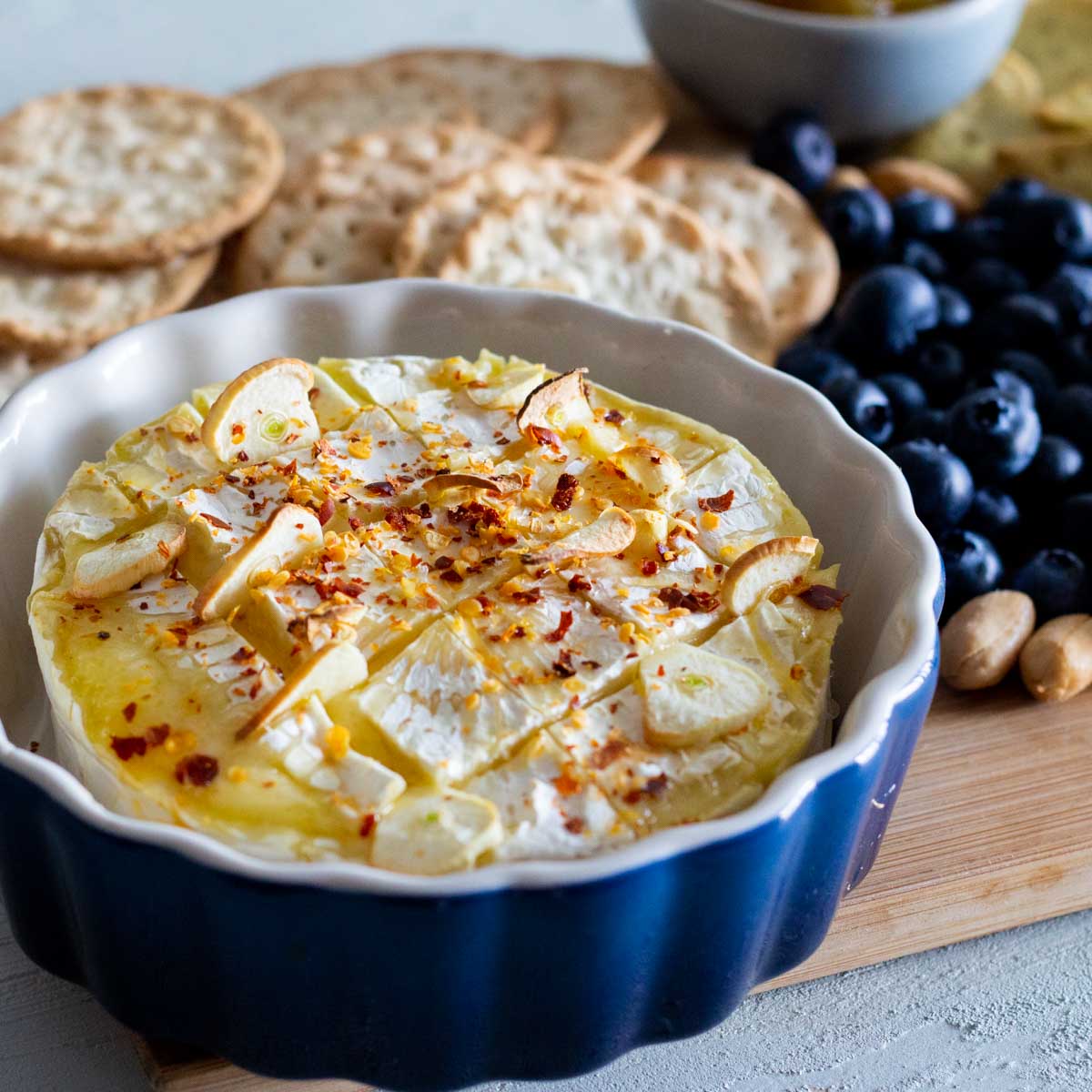 Baked brie with garlic and chili in a cheese board which has blueberries, crackers and nuts.