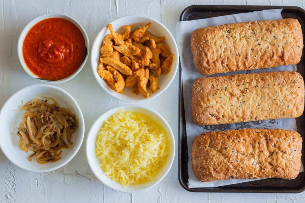 Ingredients laid out for chicken tikka bread pizza - grilled chicken, onions, caramelized onions, tomato sauce, cheddar cheese an Turkish bread.