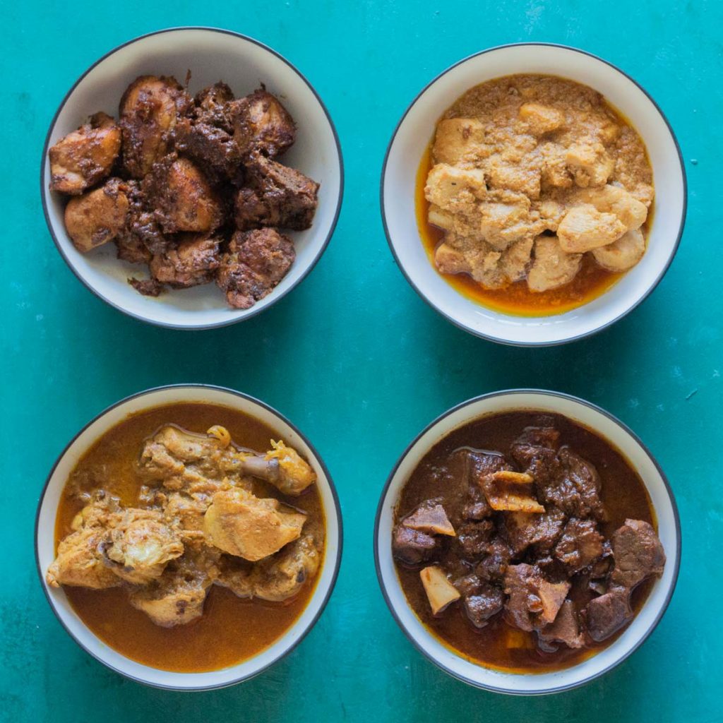 Four white bowls with blue rims. Clockwise from the top is dry chicken curry, boneless chicken curry (chicken ka salan), goat meat / mutton ka salan, and then bone in chicken ka salan.