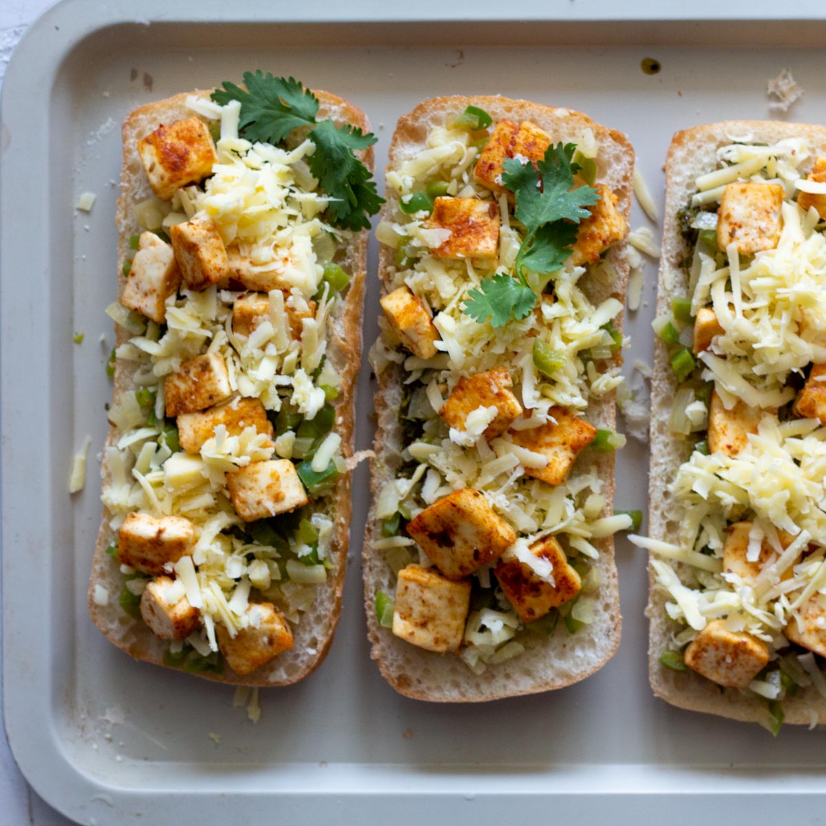 Three paneer tikka sandwiches laid out on a baking tray.