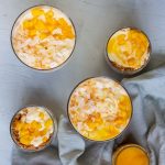 On the top left is a top down shot of a bowl of no bake mango cheesecake. Next to it is no bake mango cheesecake in a jar, and on the bottom there is a trifle bowl with another glass jar topped with biscuit crumbs and chopped mango. On the bottom right is a jar of mango puree.