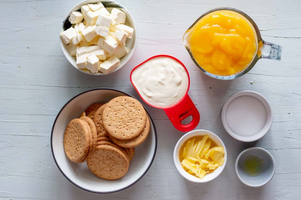 Ingredients for no bake mango cheesecake. From the top clockwise is diced cream cheese, cream, mango puree, sugar, lemon juice, butter and digestive biscuits.