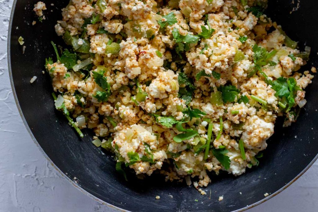 A large black wok filled with paneer samosa filling. The filling has grated paneer, coriander leaves, grated cheese, onion and spices. 