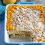 Mango coconut trifle or mango coconut layered dessert in a blue dish. The bottom left of the dish has a piece of the trifle taken out.