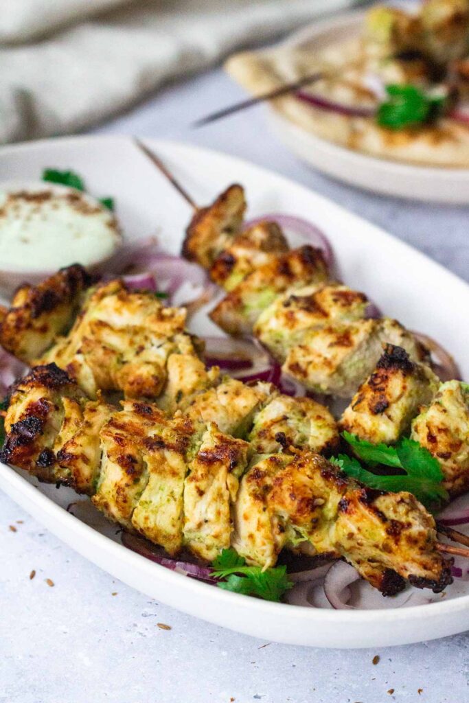 Chicken malai tikka skewers on a white serving plate.