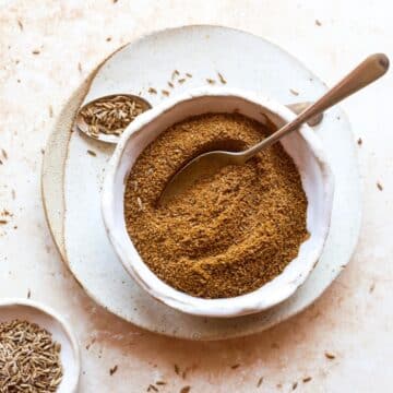 A bowl of roasted ground cumin with a spoon, on a white plate.